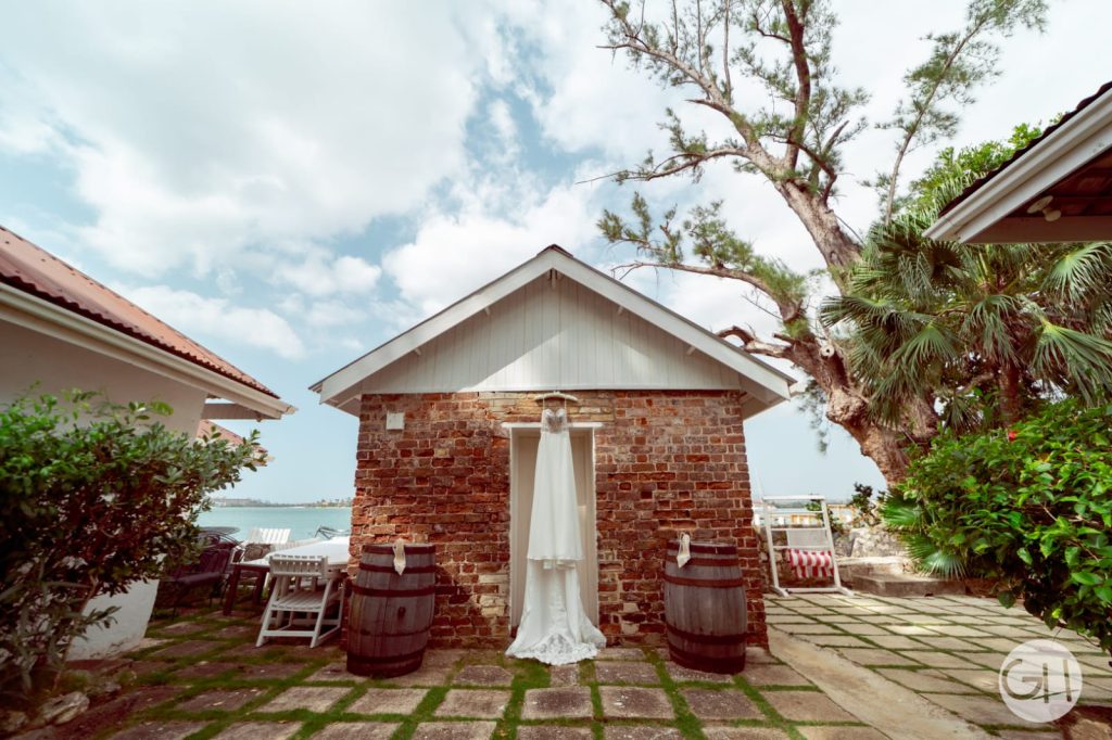 Bridal gown hanging in a rustic brick doorway at the warf house venue in montego bay by DWEPP Jamaica captured by Geovanni Hinds