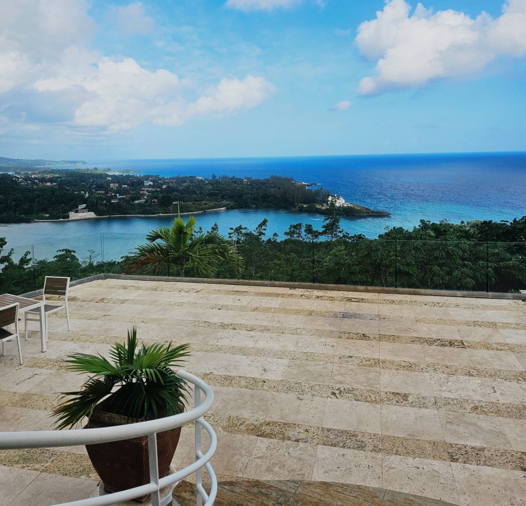 High-end travertine stone terrace with a glass railing overlooking the panoramic ocean view in Portland, Jamaica by DWEPP Jamaica
